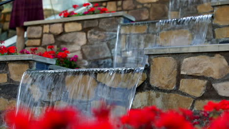 defocus view of red poppy flowers with waterfall feature on stone wall in the background