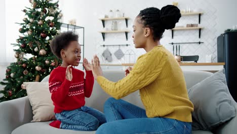 Portrait-Of-Happy-Beautiful-Woman-Playing-With-Little-Kid-While-Sitting-On-Sofa-In-Christmassy-Decorated-Room-Side-View-Of-Loving-Mom-And-Child-Spending-Time-Together-Holidays-Concept