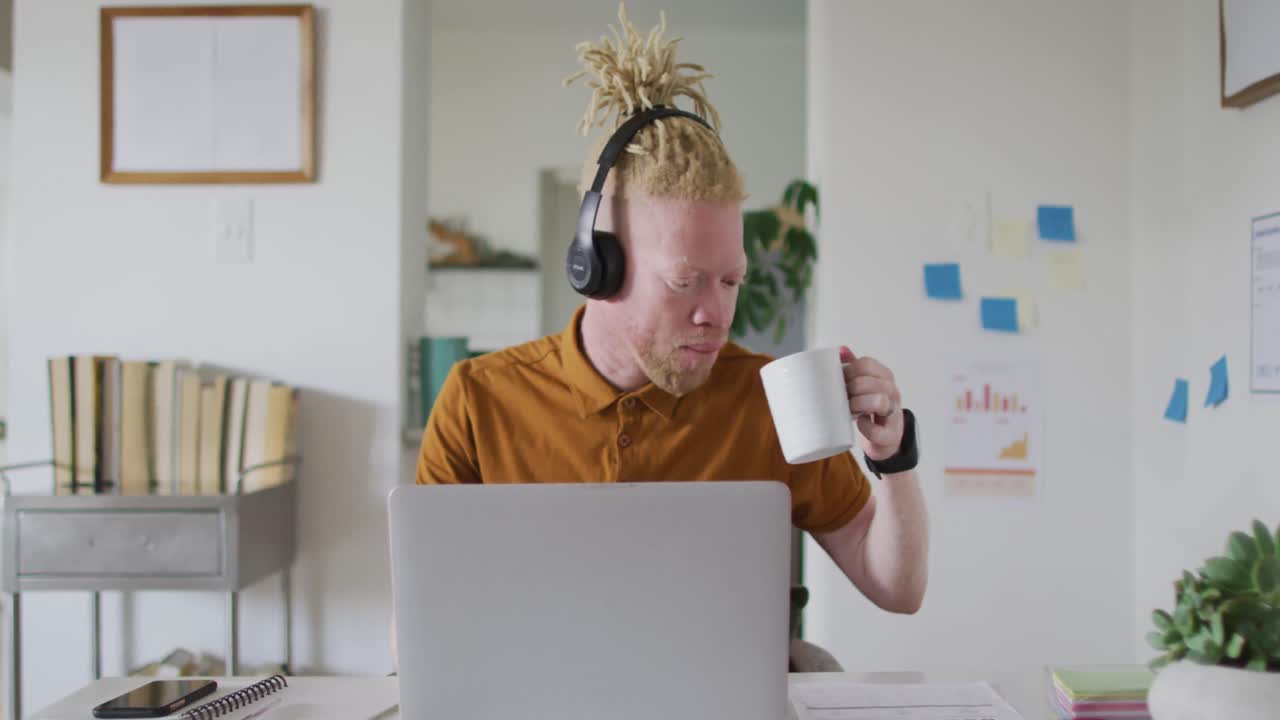 Albino african american man with dreadlocks drinking coffee making video call on the laptop