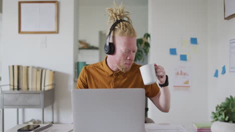 Albino-african-american-man-with-dreadlocks-drinking-coffee-making-video-call-on-the-laptop