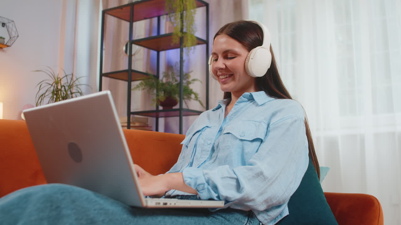 mujer feliz con auriculares inalámbricos acostada en el sofá de casa escuchando música trabajando en una computadora portátil relajándose