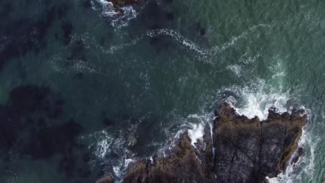 a birds-eye drone video looking down towards some large rocks above the ocean