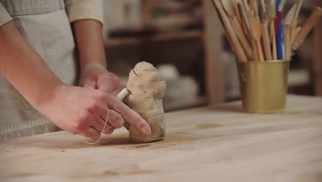 joven alfarera trabajando en un estudio de arte - cortando las piezas de arcilla usando una cuerda