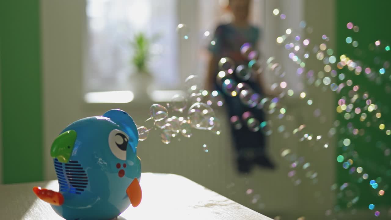 Close-up of a plastic device in a form of a fish producing soapy bubbles. Bubble blower on the table in the room with a boy who is watching at the bubbles show.
