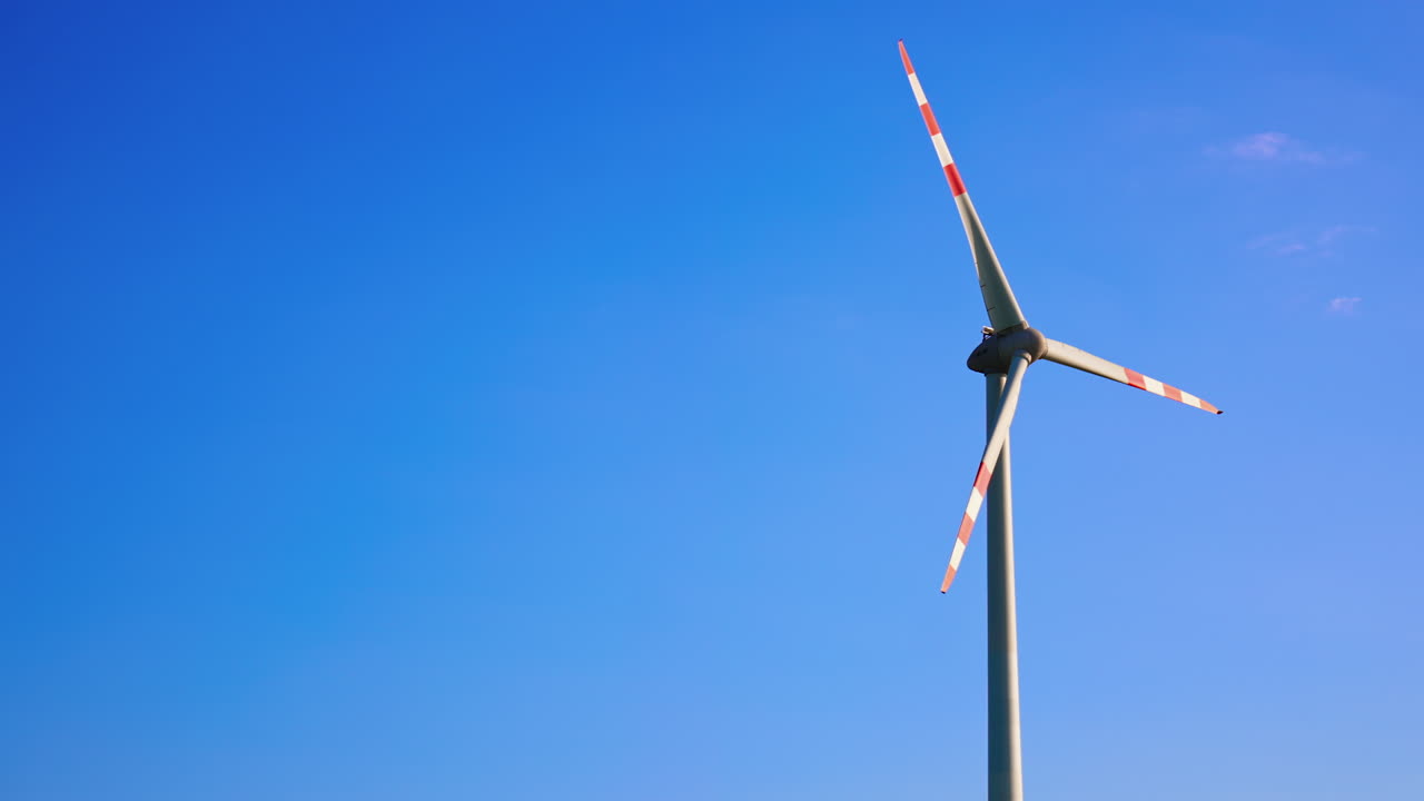Tall wind turbine in blue sky. A wind turbine rotates in the bright sunlight, showcasing renewable energy in a clear blue sky on a sunny day