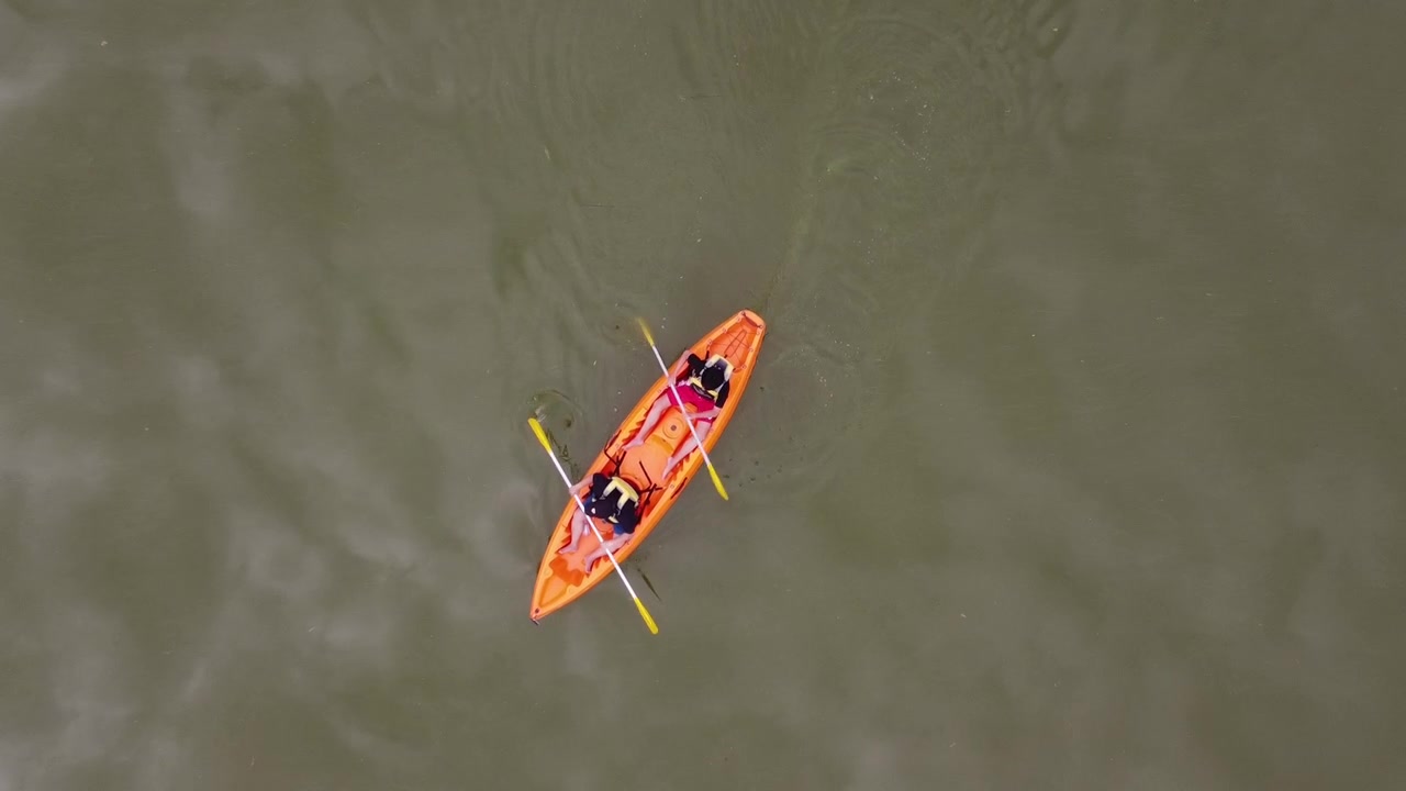 Luchtfoto van bovenaf van twee mensen die kajakken op kalm water in een feloranje kajak. Concept van avontuur en buitenrecreatie vastgelegd door drone, met nadruk op peddelen, teamwork en vredige natuur