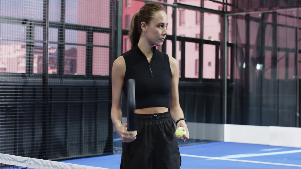 Young woman holding padel racket on court, preparing for match with focus, copy space