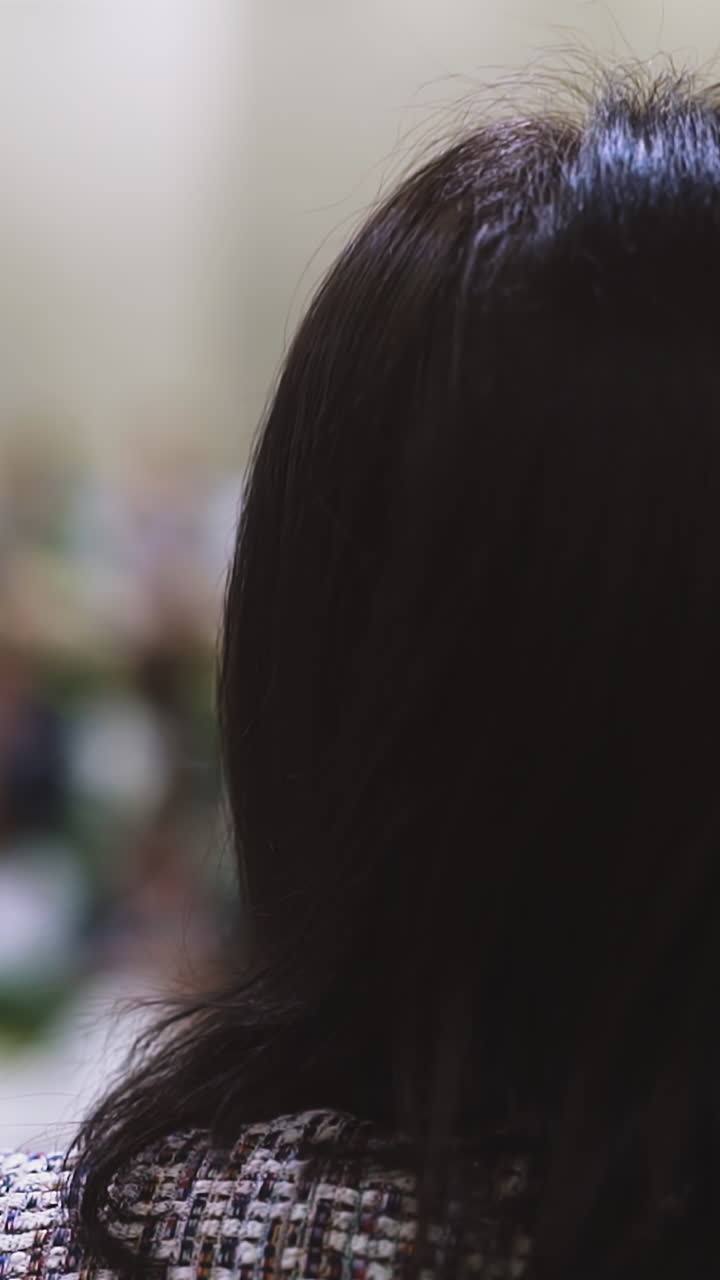 CU shot, slow motion: short haired brunette female client waits for haircut in armchair in modern brightly lit beauty salon backside close view