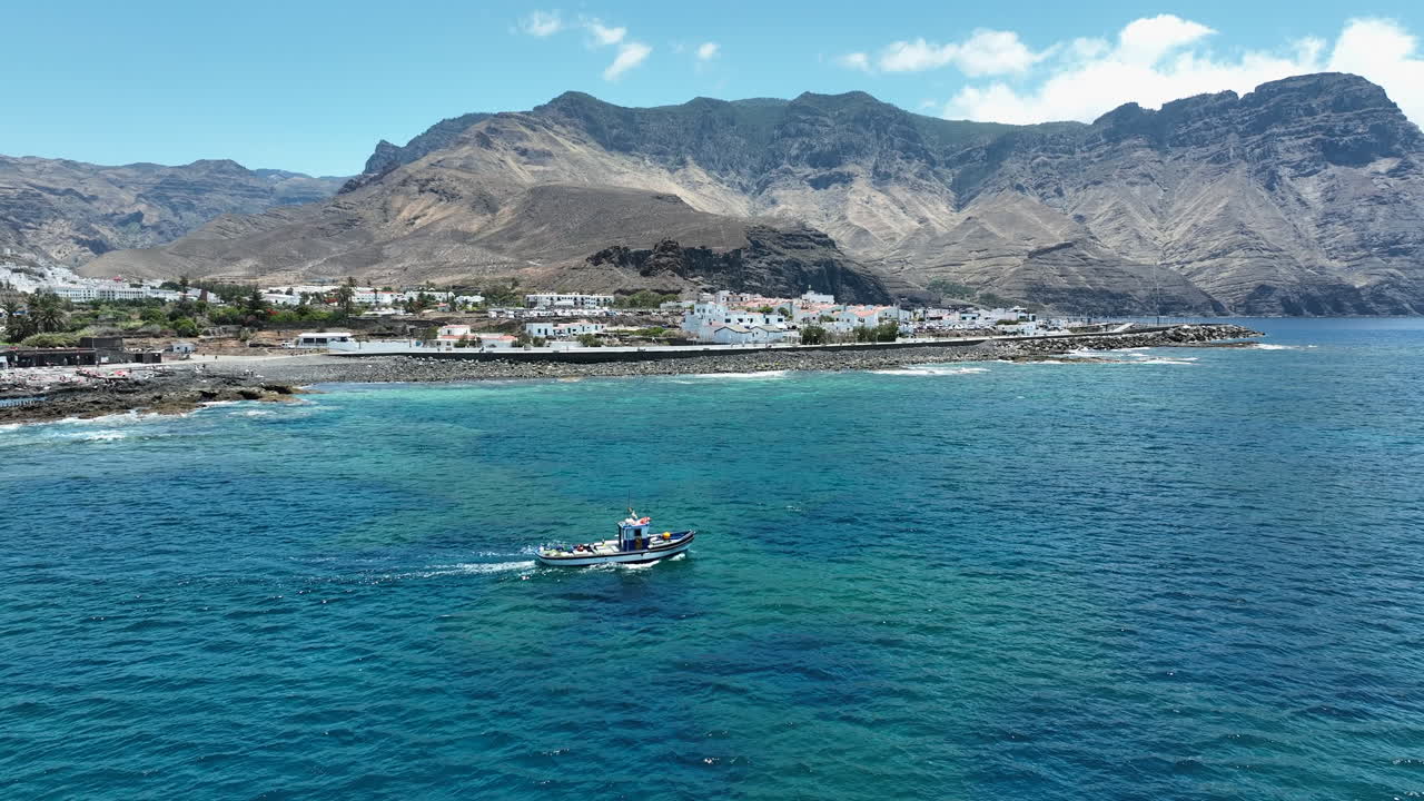 Wonderful aerial shot following a fishing boat that is in the waters of the port of Agaete and where the houses of the area can be seen