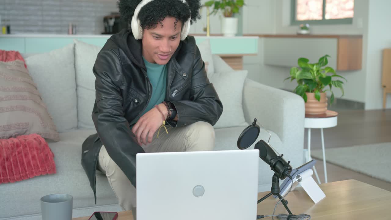 Opening laptop male podcaster adjusting microphone sipping mug and preparing recording on home sofa