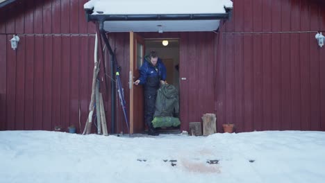 man coming out the door carrying heavy camping bag