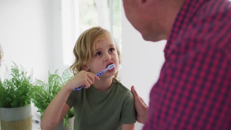 abuelo caucásico ayudando a su nieto a cepillarse los dientes en casa