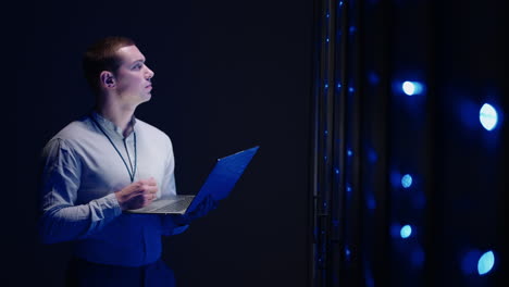 concept of digitalization of information: it specialist in front of server racks with laptop activates data center with a touch gesture. working on a laptop standing before open server rack cabinet