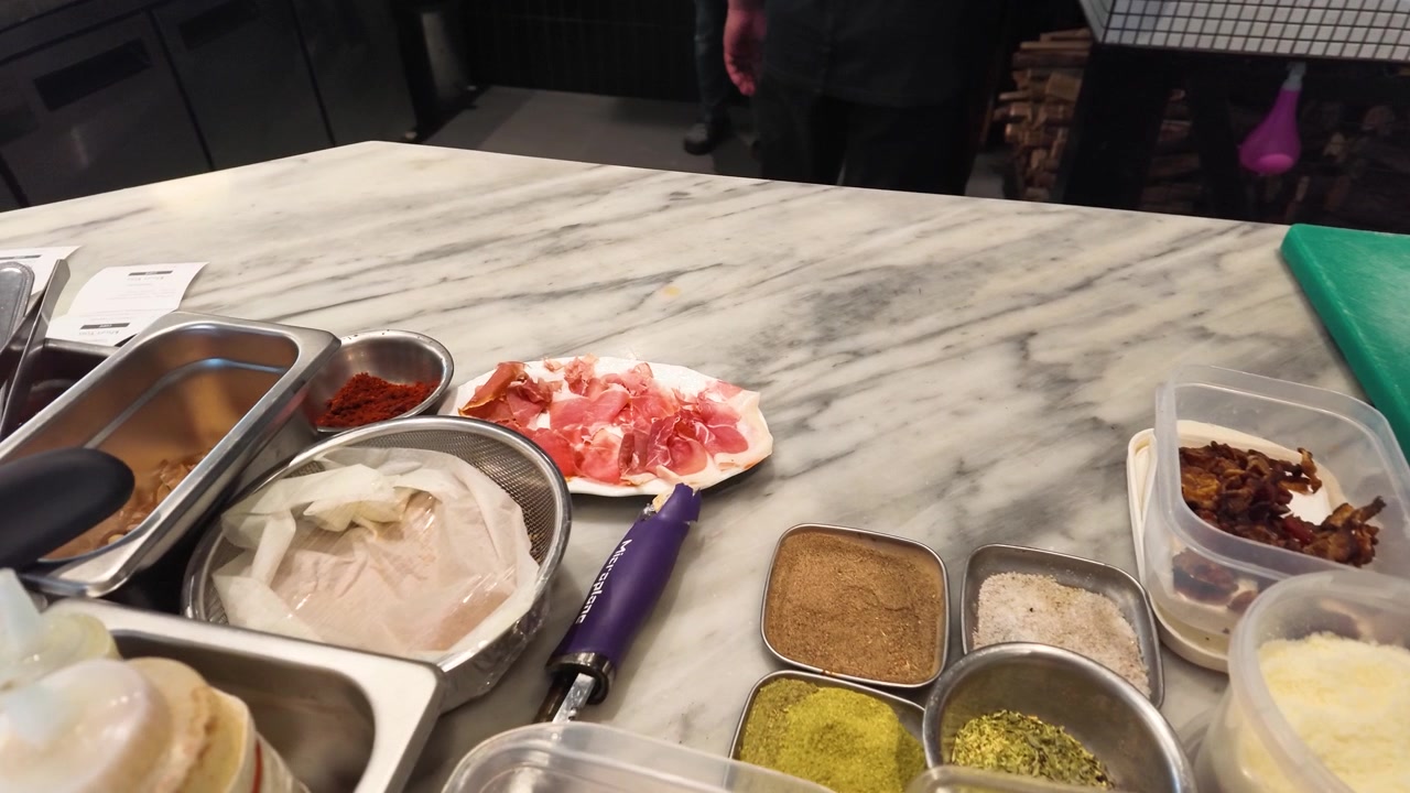 Close-up shot of fresh prosciutto, spices, and dough organized for gourmet pizza preparation.