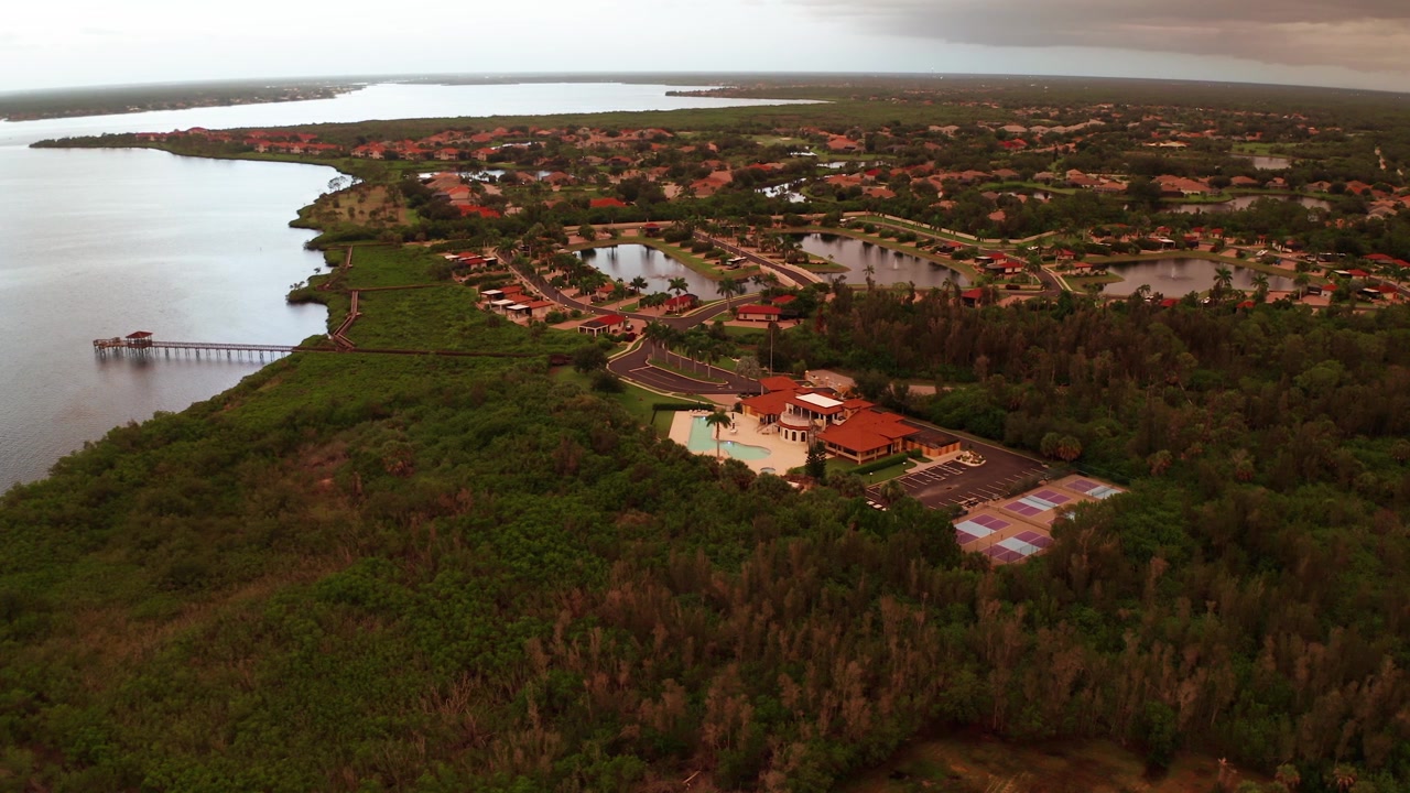 Planlagt søsidekvarter, klubhus og lang træpromenade ligger ved en skovklædt flodmunding, mens kameraet svæver højt over ved skumringstid