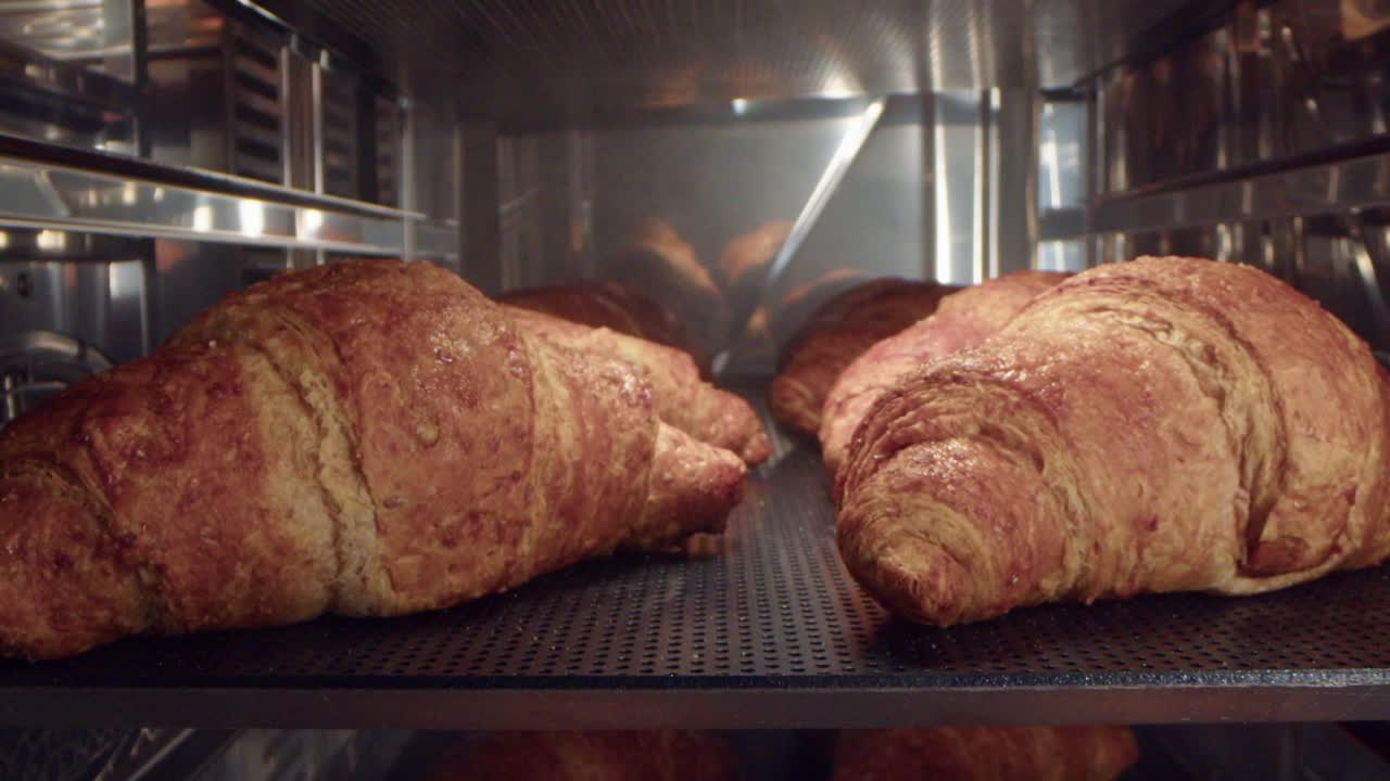 la cámara retrocede a una vista en primer plano de capas de croissants dorados y escamosos recién horneados en el horno.