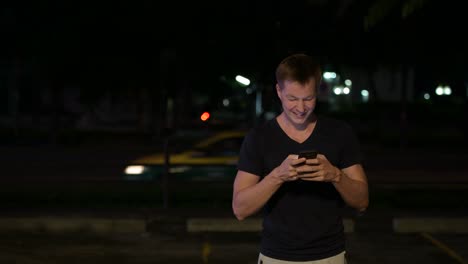 joven escandinavo guapo usando el teléfono en las calles por la noche