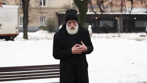 An elderly man standing outside has chest pains or a heart attack. Stroke in winter. Healthcare concept.