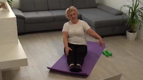 deporte en casa. mujer mayor activa haciendo ejercicios de estiramiento de calentamiento frente a una computadora portátil, entrenando con tutoriales en línea