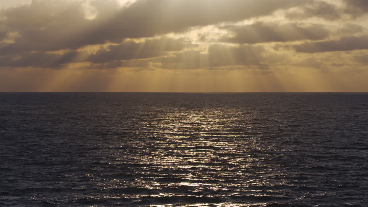 Serene ocean at sunset with soft colors reflecting on the water, sun rays peeking through clouds
