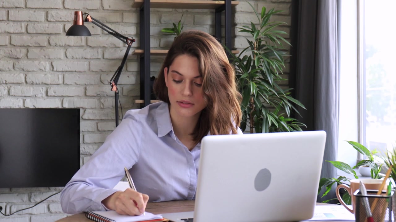 Jovem trabalhando no laptop e fazendo anotações em um escritório moderno