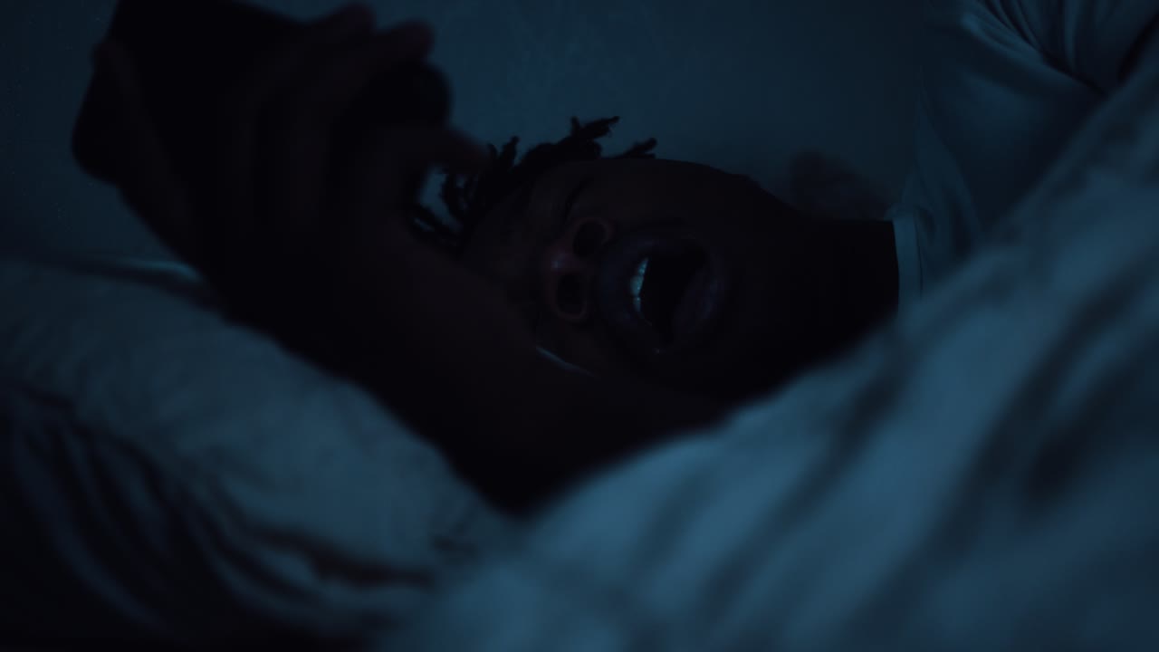 hombre cansado usando un teléfono inteligente mientras está acostado en la cama tarde en la noche