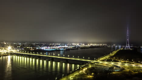 vehículos que conducen a través del puente de carretera sobre el río daugava cerca de la torre de radio y televisión de riga por la noche