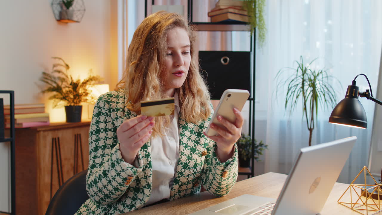 Smiling woman using bank credit card and smartphone for online shopping payments at home office