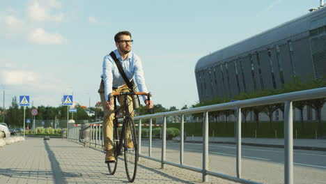 homem bonito usando fones de ouvido, usando óculos e um estilo casual e andando de bicicleta