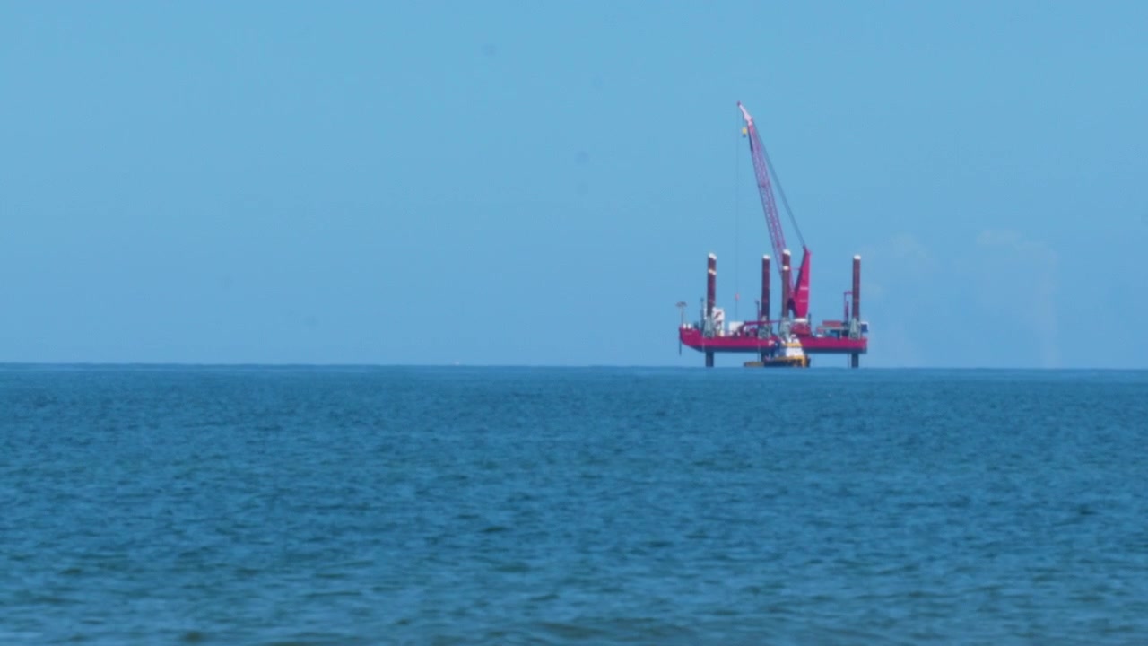 A red industrial jackup rig or offshore platform with a crane positioned in the open blue sea. Suitable for energy industry, oil exploration, and sustainability transition projects.