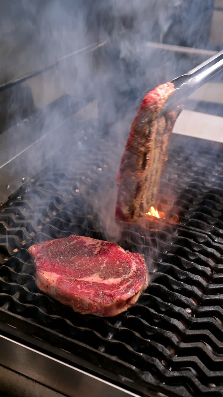 Steaks cooking on the grill with smoke rising. Two beef steaks cooking on the grill with smoke and seasoning on the surface