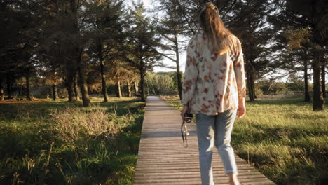 Young-woman-and-her-dog-walking-on-a-boardwalk-in-a-national-park-while-sunset