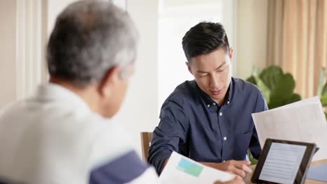 diverse financial advisor and senior man discussing paperwork and using tablet at home, slow motion