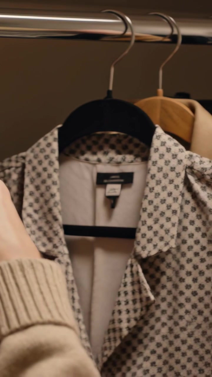 Video verticale: Aprendo un armadio, un braccio e una mano con un capo in maglia beige scorrono sull'asta, controllando una camicia a fantasia.