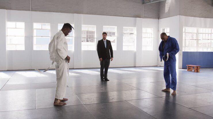 Nel dojo, praticanti di judo che si legano le cinture con l'istruttore che osserva, preparandosi per la lezione