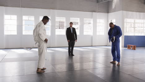 in dojo, judo practitioners tying belts with instructor observing, preparing for class