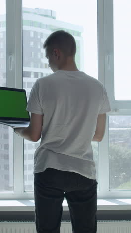 joven trabajando en una computadora portátil junto a la ventana