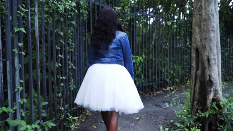 african american woman walking down wooded park path in white dress and jacket in cinematic 4k 60fps