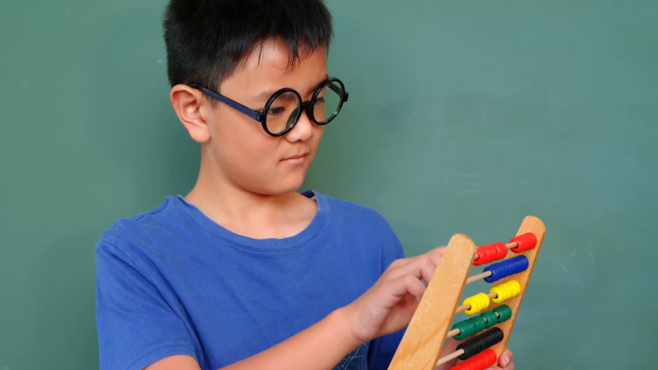Vista frontale di uno scolaro asiatico che risolve un problema di matematica con un abaco in un'aula a scuola 4k