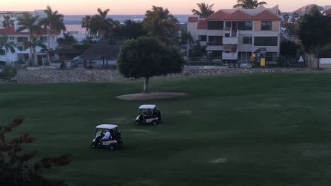 men driving two golf carts across a golf course early in the morning in san jose del cabo, mexico