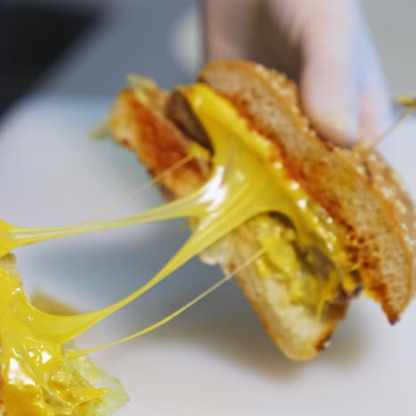 cutted in a half tasty appetizing cheesburger. chef in gloves shows a hamburger with meat cutlet and cheese