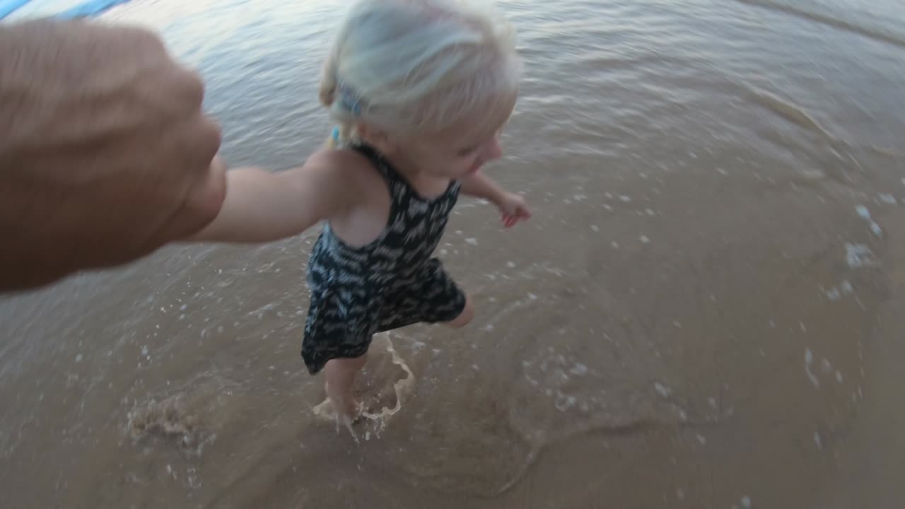 아기 소녀는 해가 지는 모래 해변에서 아버지에 의해 회전합니다.