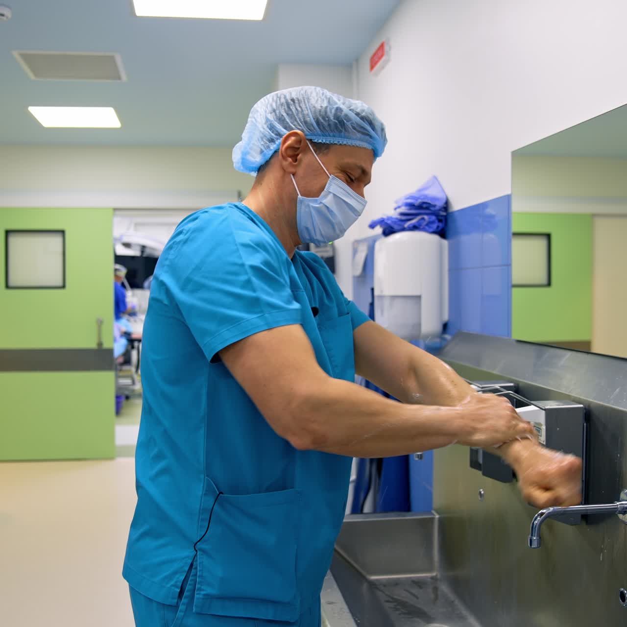 Un cirujano sonriente y positivo se lava las manos cuidadosamente en la sala preoperatoria. El doctor se prepara para la operación.