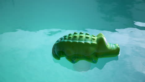 Green-crocodile-chlorine-dispenser-floating-on-clear-turquoise-water-in-a-swimming-pool