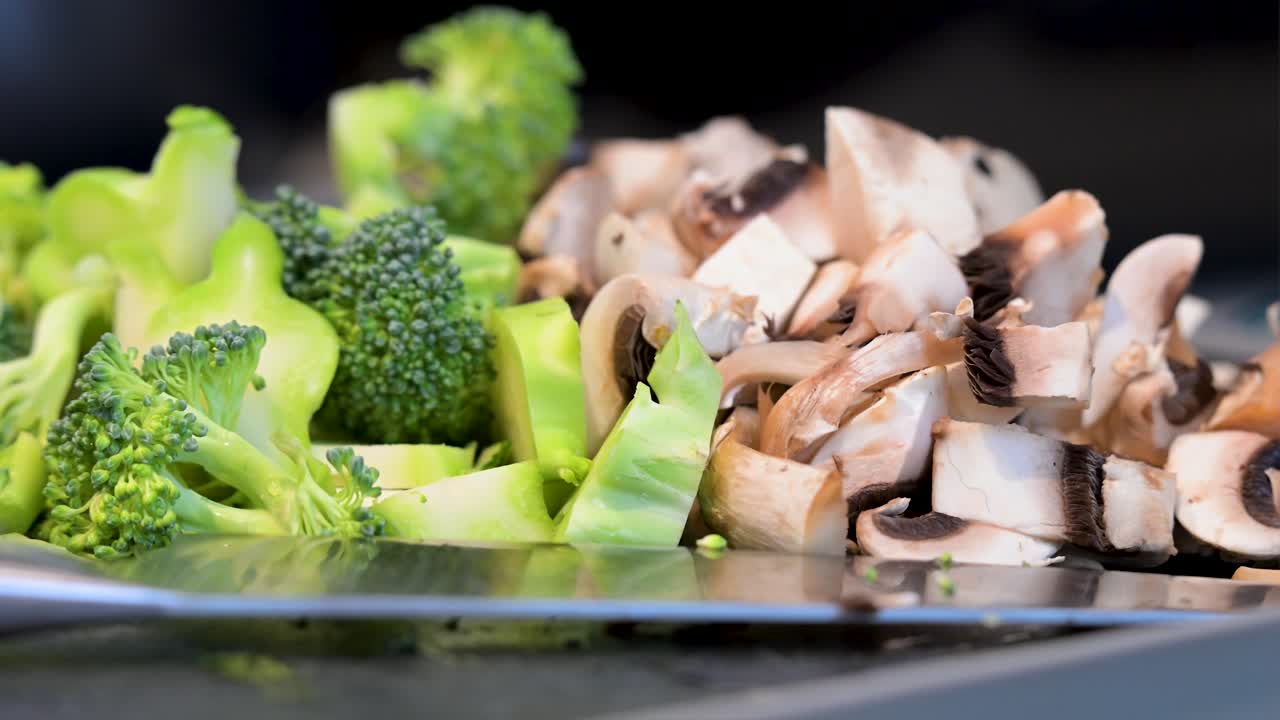 A close-up view of vibrant green broccoli florets and sliced mushrooms on a dark surface. The fresh, healthy ingredients are prepared for use in a culinary dish
