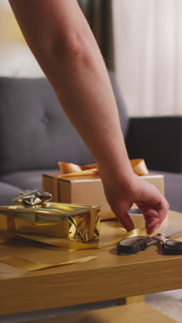 vertical video of man wrapping gift or present on table at home with scissors sticky tape and ribbon