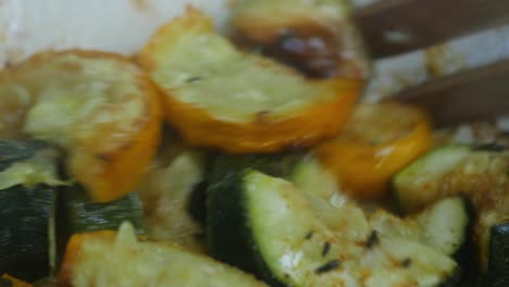 steaming close up of oven roasted green and yellow courgettes seasoned with thyme, salt and habanero chili powder, gently stirred around with a wooden fork