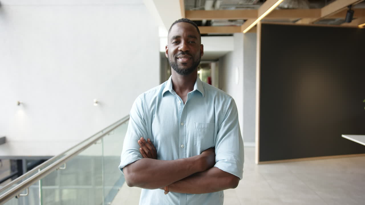 Confident businessman standing with arms crossed in modern office hallway