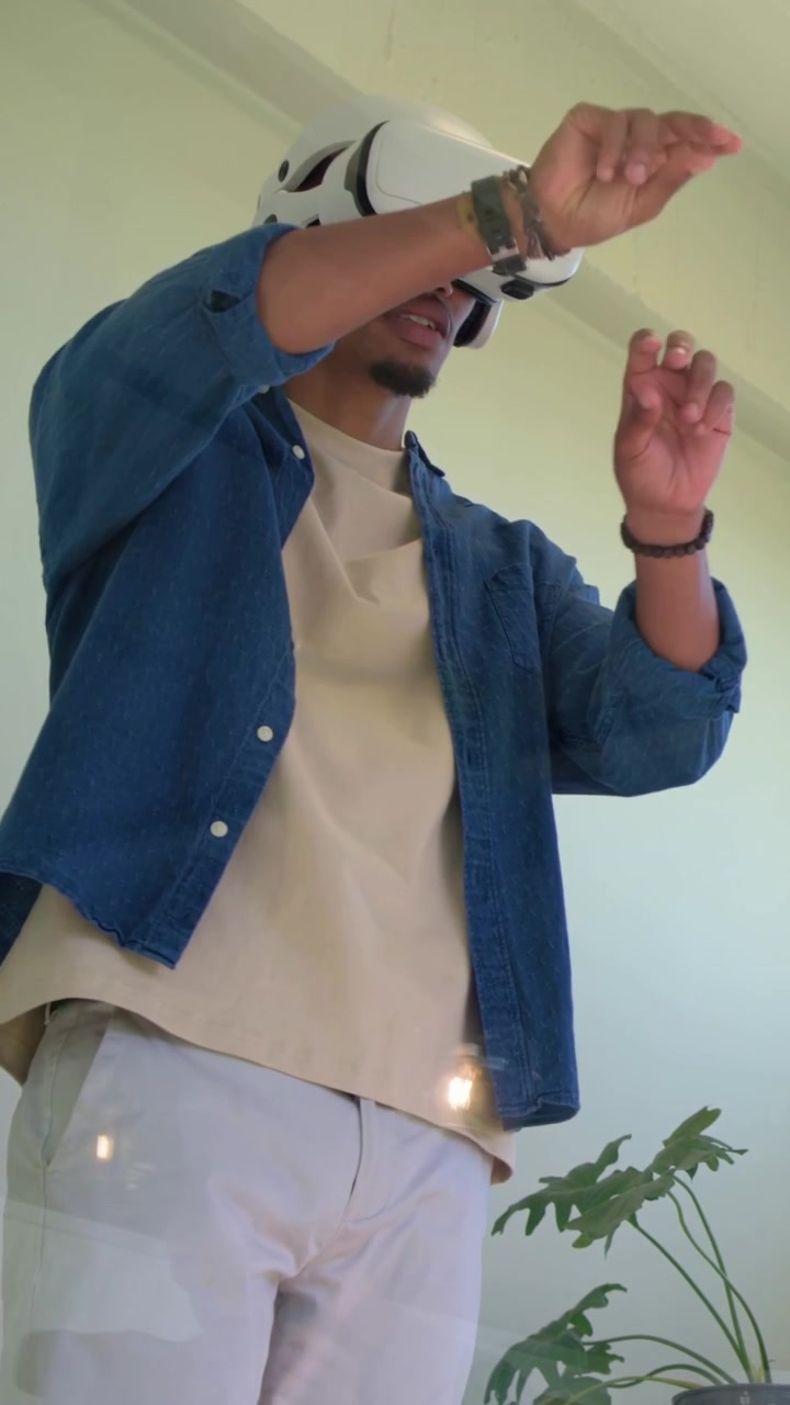 Vídeo vertical: Headset ativando, homem usando headset VR branco e camisa jeans percorrendo o cômodo.