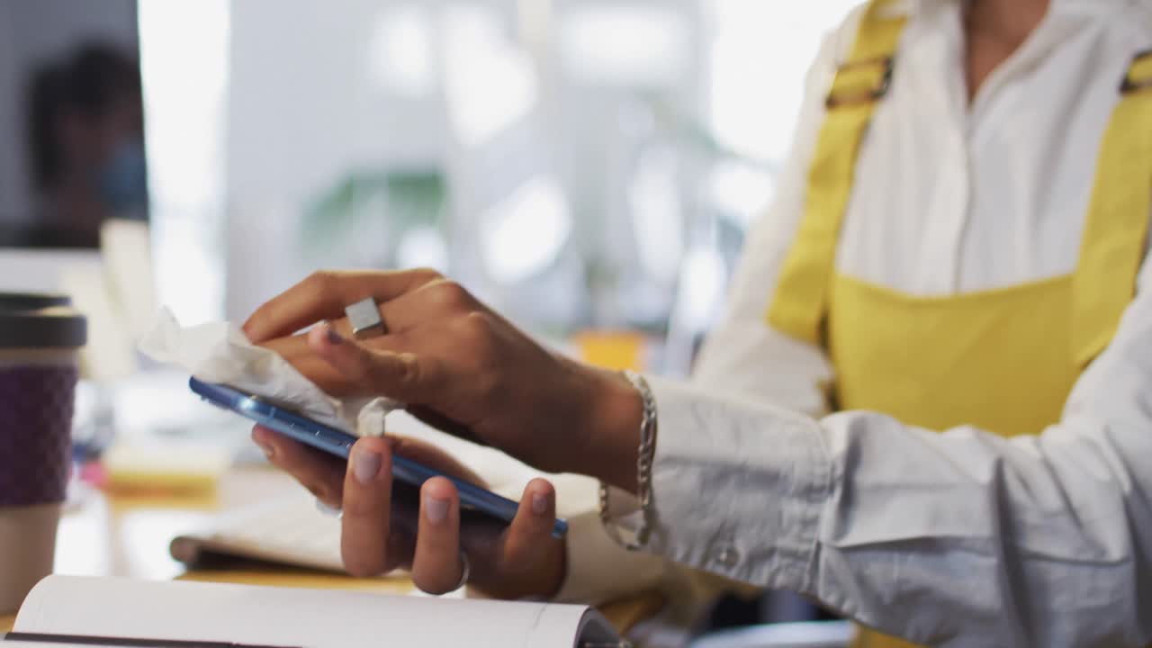 Woman wearing face mask wiping her smartphone with a tissue